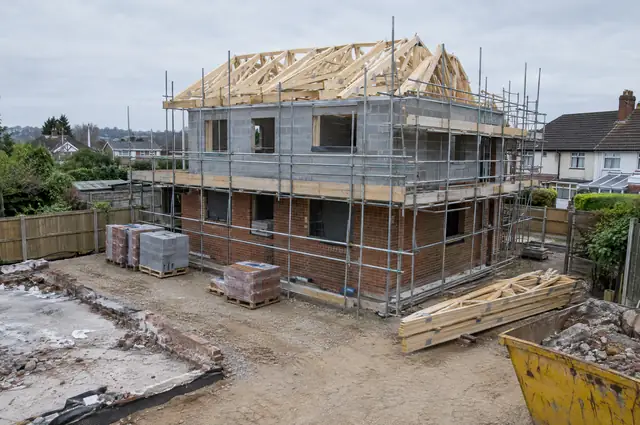 New house under construction with scaffolding and roof trusses on a cleared plot